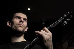 uma homem tocam a guitarra. face do uma homem com uma musical instrumento em uma Sombrio fundo. foto