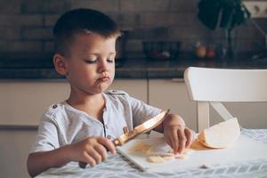 fofa Garoto 4-5 anos velho com faca corte uma queijo em a corte borda em a mesa dentro a cozinha foto