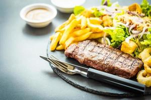 Bife de carne grelhada com batata frita anel de cebola com molho e vegetais frescos foto