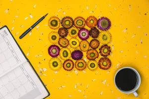 topo Visão conceito do pastel amarelo fundo, colorida flores este estão arranjado dentro uma retangular forma com uma caderno, caneta e copo do café colocada. conceito, escrever uma observação, natureza, livro. foto