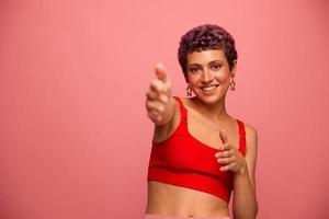 moda retrato do uma mulher com uma curto corte de cabelo do roxa cor e uma sorrir com dentes dentro uma vermelho topo em uma Rosa fundo felicidade foto