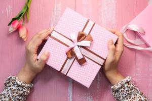 mãos segurando uma caixa de presente rosa foto