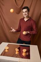 alegre homem dentro uma vermelho camisa com laranjas dentro dele mãos uma espelho em a mesa foto