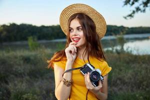 mulher com uma Câmera dentro dela mãos vestindo uma chapéu vermelho lábios Veja a parte, de lado natureza foto