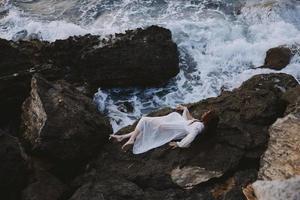 sensual mulher dentro uma isolado local em uma selvagem rochoso costa dentro uma branco vestir panorama foto