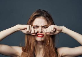 mulher com vermelho lábios chorando em cinzento fundo e mãos perto face cortada Visão foto