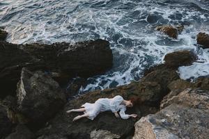 lindo mulher dentro uma isolado local em uma selvagem rochoso costa dentro uma branco vestir período de férias conceito foto