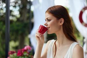 retrato do jovem lindo mulher com vermelho copo do café ao ar livre cafeteria inalterado foto