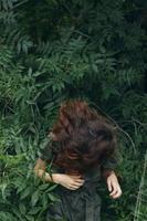 retrato do uma mulher inclinou-se frente e a verde folhas do a arbustos natureza viagem foto