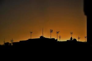 pitoresco panorama às pôr do sol com Preto telhados do casas e antenas foto