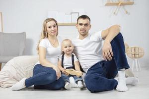 família. Papai mãe criança sentar em a chão às lar. retrato marido esposa e pequeno filho. casal com bebê dentro a apartamento foto