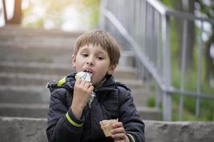 uma criança em a rua come gelo creme. Garoto com uma doce sobremesa dentro a parque. foto
