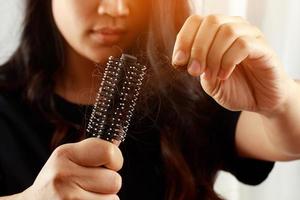 vista traseira jovem preocupada com problema de perda de cabelo, desequilíbrio hormonal, conceito de estresse. muitos cabelos caem depois de pentear na escova de cabelo na mão. fêmea desembaraçou o cabelo com um pente, cuidados de saúde foto