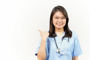 mostrando e apontando produtos com polegar do ásia jovem médico isolado em branco fundo foto