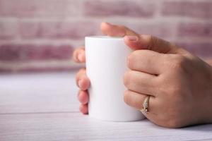 feche a mão de uma mulher segurando uma xícara de café de cor branca foto