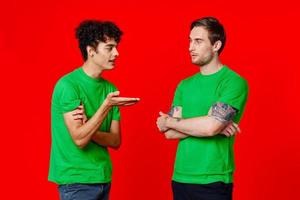 dois amigos dentro verde Camisetas estão em pé lado de lado comunicação positivo vermelho fundo foto