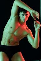 masculino atleta em uma Sombrio fundo posando e mostrando músculos em a abdômen foto