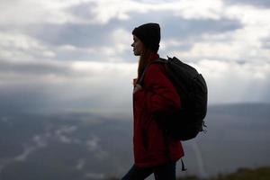 mulher viaja dentro a montanhas com uma mochila dentro a tarde panorama nuvens clima foto