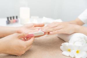 mulher recebe serviço de atendimento por manicure esteticista profissional no centro de spa. salão de beleza de unhas usa lixa de unha para tratamento de esmalte. manicure faz cliente de unha bonita. tratamento de spa para cuidados com o corpo foto