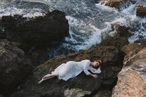 lindo jovem mulher dentro uma isolado local em uma selvagem rochoso costa dentro uma branco vestir panorama foto