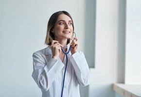 mulher com profissional estetoscópio médico dentro médico vestido dentro brilhante quarto foto