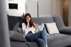 mulher com uma telefone dentro dela mãos sentado em a sofá dentro a apartamento às casa descansar foto