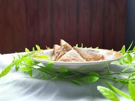 indonésio vegetal sambusa com carne peixe o preenchimento em uma mini placa. uma sambusa ou samosa é uma frito ou cozido prato com uma salgado enchimento, tal Como União, carne peixe, e outros. foto