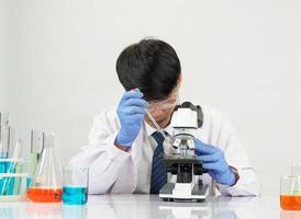 ásia masculino aluna cientista vestindo uma médico vestido dentro a laboratório olhando mão às químico. causou de mistura reagentes dentro científico pesquisa laboratórios com teste tubos e microscópio em a mesa foto