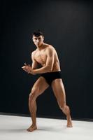 comprimento total desportivo homem com muscular corpo dentro Preto calcinhas posando contra uma Sombrio fundo foto