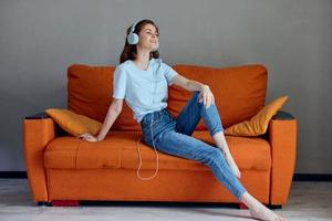 lindo mulher sentado em a sofá às casa ouvindo para música em fones de ouvido estilo de vida foto