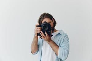 uma masculino hipster fotógrafo dentro uma estúdio contra uma branco fundo parece através a Câmera visor e fotos tiros com natural luz a partir de a janela. estilo de vida trabalhos Como uma freelance fotógrafo