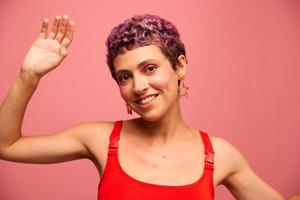 moda retrato do uma mulher com uma curto corte de cabelo do roxa cor e uma sorrir com dentes dentro uma vermelho topo em uma Rosa fundo felicidade foto