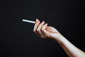 mão feminina segurando um cigarro em um fundo escuro foto