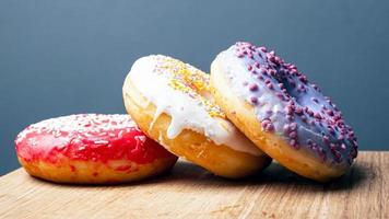 donuts com cobertura multicolorida vermelha, branca e roxa em um suporte de madeira sobre um fundo cinza foto