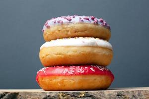 três donuts com esmalte colorido de vermelho violeta e branco com pó foto