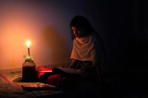 uma jovem menina estudando às casa com luz de velas depois de eletricidade carga derramamento às dhaka cidade. foto