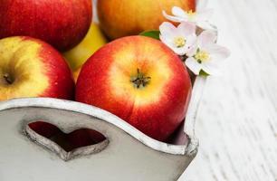 caixa com maçãs e flores de macieira em uma mesa de madeira foto