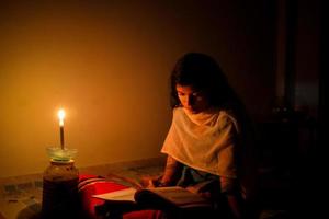 uma jovem menina estudando às casa com luz de velas depois de eletricidade carga derramamento às dhaka cidade. foto