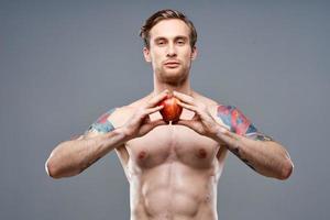 masculino atleta com a maçã dentro dele mãos e tatuagem cubos em dele estômago bíceps pressione foto