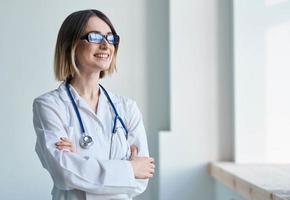 profissional médico mulher com óculos perto janela e estetoscópio foto