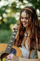 feliz hippie mulher com uma guitarra relaxante dentro natureza sentado em uma xadrez sorridente e desfrutando a visualizar. estilo de vida dentro harmonia com natureza e auto foto