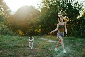 mulher e dela rouco cachorro alegremente corrida através a Relva dentro natureza dentro a parque sorrir com dentes outono andar com bicho de estimação, viajando com uma cachorro amigo foto