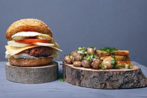 suculento hambúrguer gordo, batatas fritas e cogumelos com ervas em bandejas de madeira em fundo cinza foto