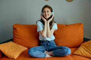 retrato do uma mulher sentado em a sofá às casa ouvindo para música em fones de ouvido estilo de vida foto