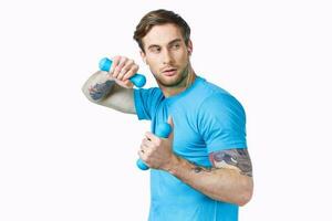 esporte homem dentro azul camiseta segurando halteres ginástica exercício cortada Visão foto