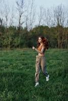 uma jovem mulher exercício lado de fora e corrida dentro a parque. dentro a tarde em a verde Relva para dentro a pôr do sol foto