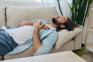 uma homem dormindo em a sofá durante a dia é cansado e relaxado depois de estresse e sentindo-me ruim. estresse às trabalhar, pobre dormir e saúde problemas foto