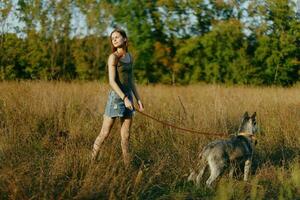 mulher e dela rouco cachorro alegremente caminhando e corrida dentro a Relva dentro a campo sorrir com dentes outono pôr do sol andar com uma bicho de estimação, viajando com uma amigo cachorro felicidade foto