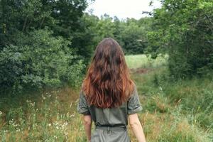 morena mulher dentro macacão em uma Prado dentro a floresta costas Visão foto