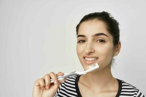 alegre mulher escova seu dentes com uma escova de dente luz fundo foto